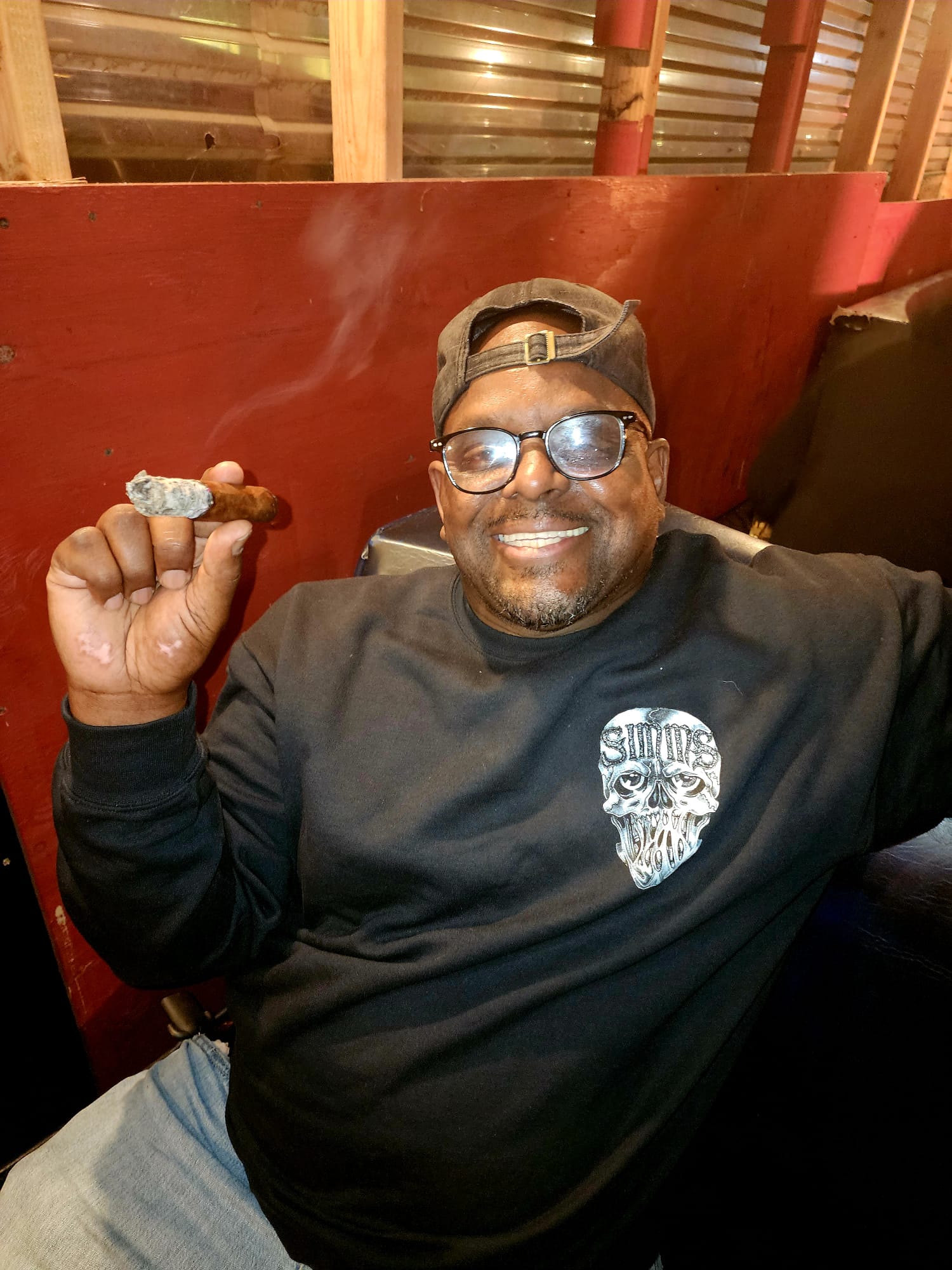 A smiling guest raises a lit cigar inside a cigar lounge.