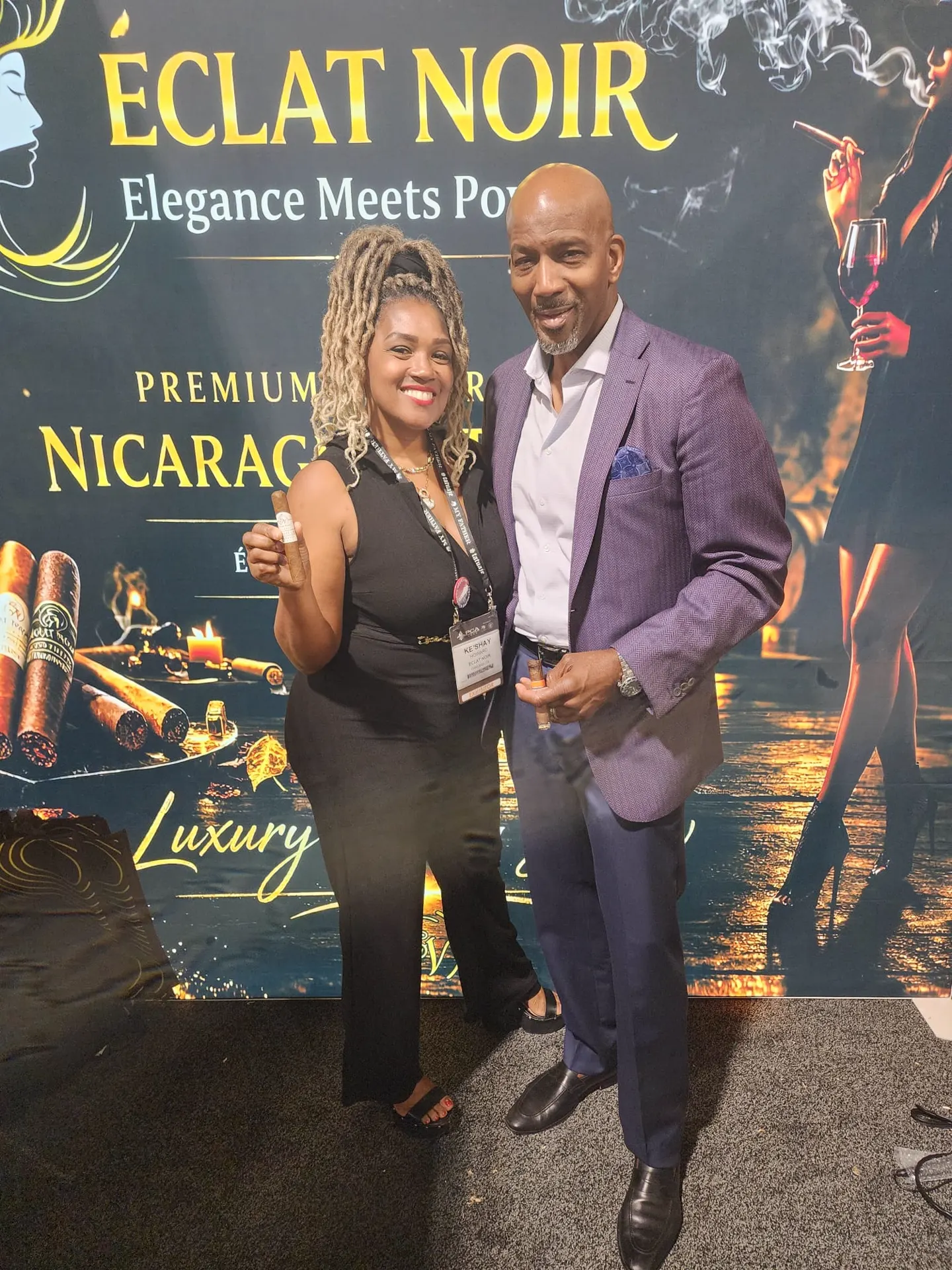 Founder and CEO L. Howard holding an ÉCLAT NOIR cigar beside an attendee in front of the booth banner, PCA Trade Show, New Orleans, April 2026.